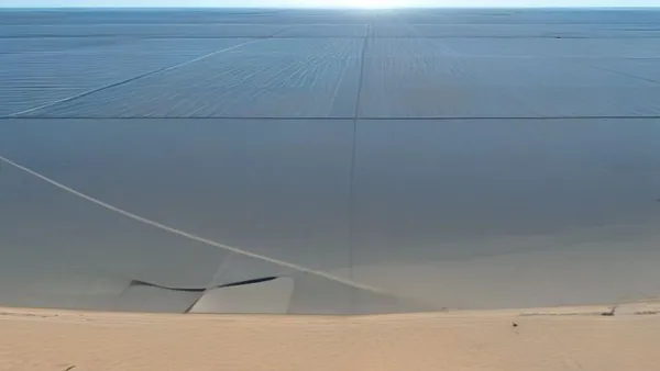 Fileiras extensas de painéis solares fixados em estrutura de rastreamento sobre terreno aberto