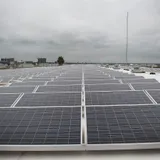 Grande arranjo de painéis solares instalados em telhado comercial sob céu nublado