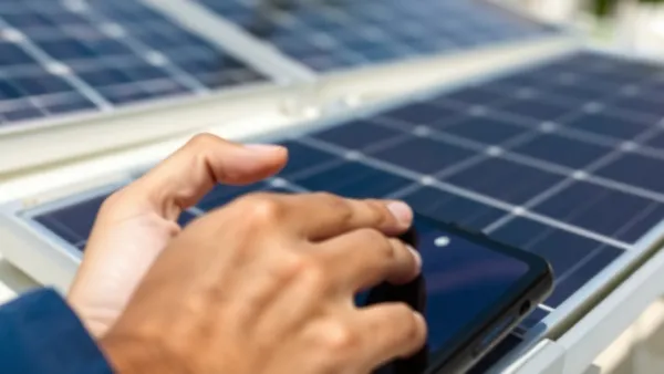 Pessoa segurando smartphone com tela de pagamento Pix em frente a telhado com painéis solares instalados