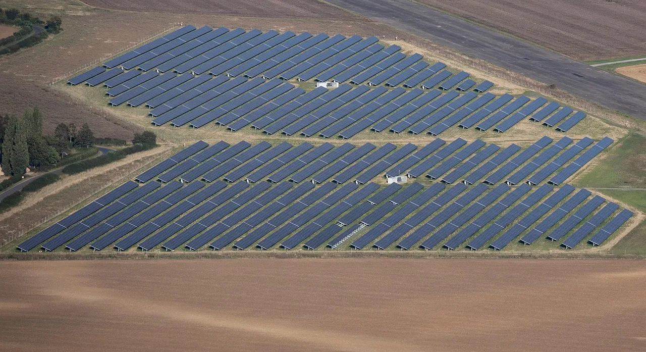 Vista aérea de usina fotovoltaica com painéis solares enfileirados sob céu parcialmente nublado